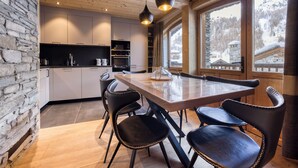 Una cocina moderna con una amplia mesa de madera y sillas, pared de piedra y ventanas grandes con vistas a un paisaje nevado.