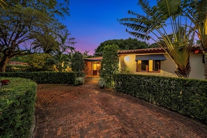 A brick pathway leading to a building with a tiled roof, surrounded by well-maintained hedges and tropical plants. - Villa Brisas in Coral Gables area (Miami)