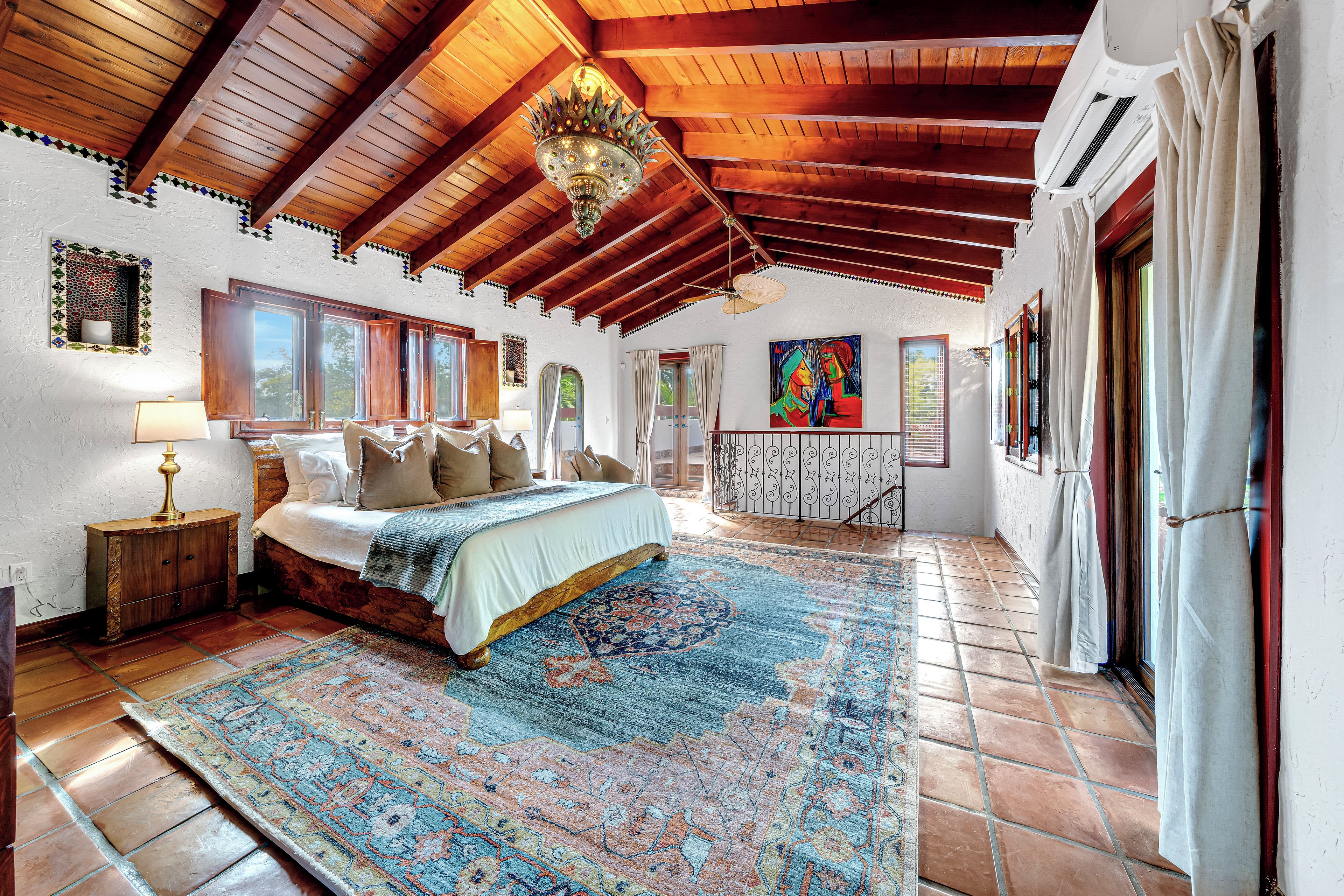 Un dormitorio amplio con una cama grande, una lámpara decorativa y vistas al exterior a través de varias ventanas.