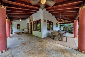 A covered outdoor seating area with a stone floor, wooden beams, and a view of the garden. - Villa Brisas in Coral Gables area (Miami)