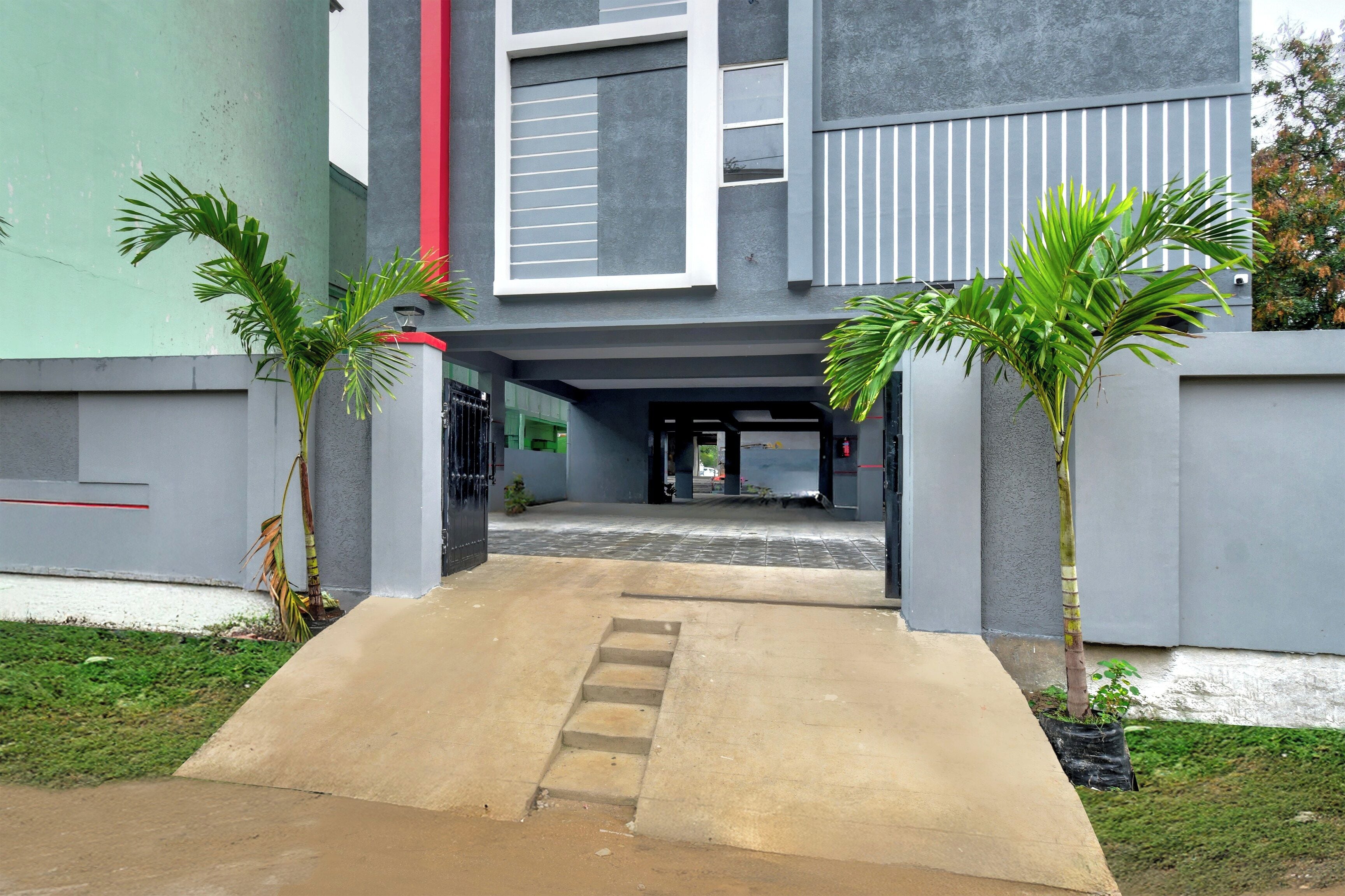 A building entrance with a concrete pathway leading to a door, flanked by two palm trees.