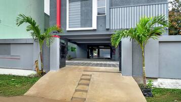 A building entrance with a concrete pathway leading to a door, flanked by two palm trees.
