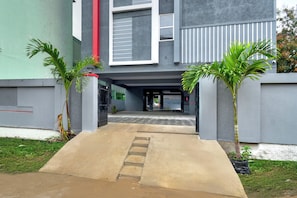 A building entrance with a concrete pathway leading to a door, flanked by two palm trees.