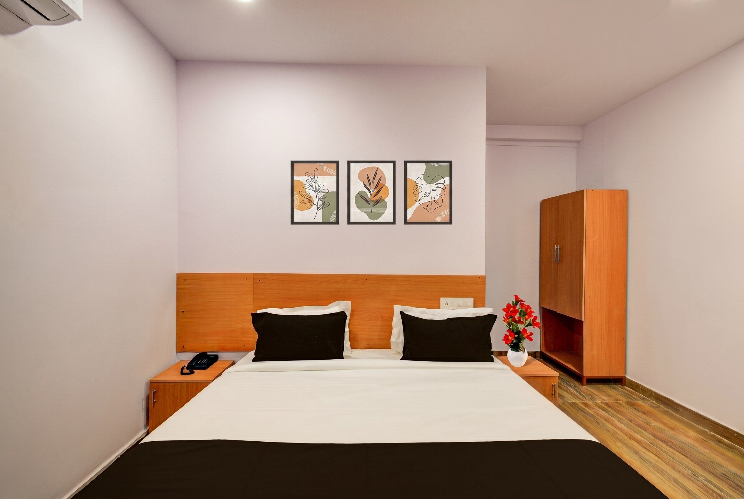 A hotel room with a bed, bedside tables, a wardrobe, and three framed artworks on the wall.