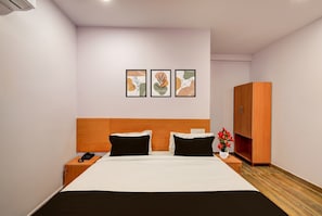 Habitación de hotel con cama, mesitas de noche, armario y tres cuadros enmarcados en la pared.