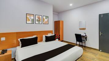 Une chambre d’hôtel comprenant un lit, un bureau avec une chaise, une armoire et trois tableaux encadrés accrochés au mur.