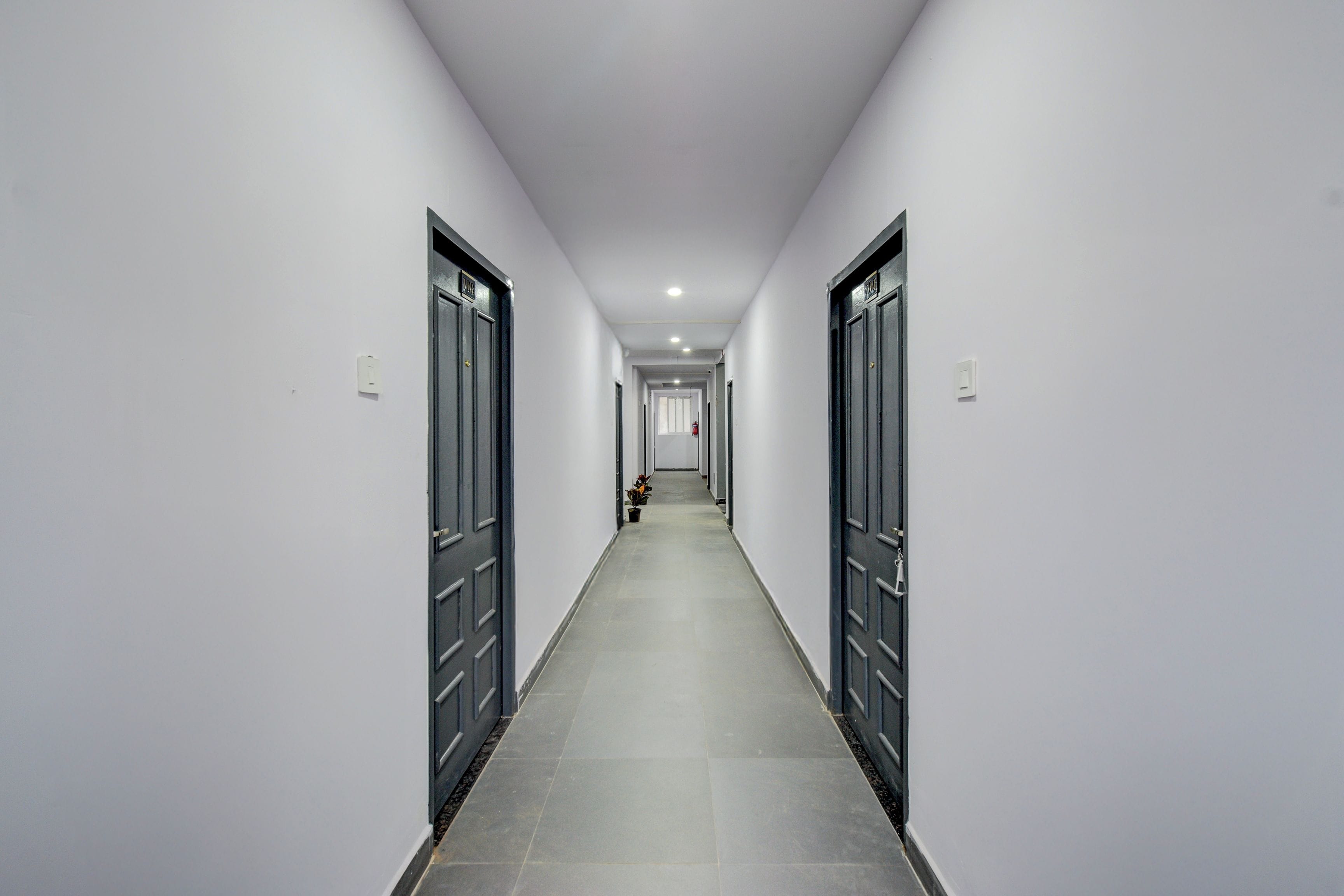Um corredor longo e estreito com portas em ambos os lados, que leva a um quarto no final.