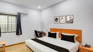 Et hotelværelse med seng, skrivebord, stol, lille bord, natbord og et spejl på væggen.