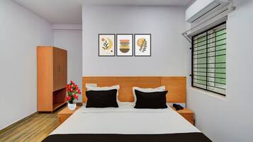 Una habitación de hotel con una cama, un armario, una mesita de noche, un jarrón con flores y tres cuadros en la pared.