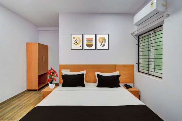 Quarto de hotel com cama, guarda-roupa, mesa de cabeceira, um vaso com flores e três quadros na parede.