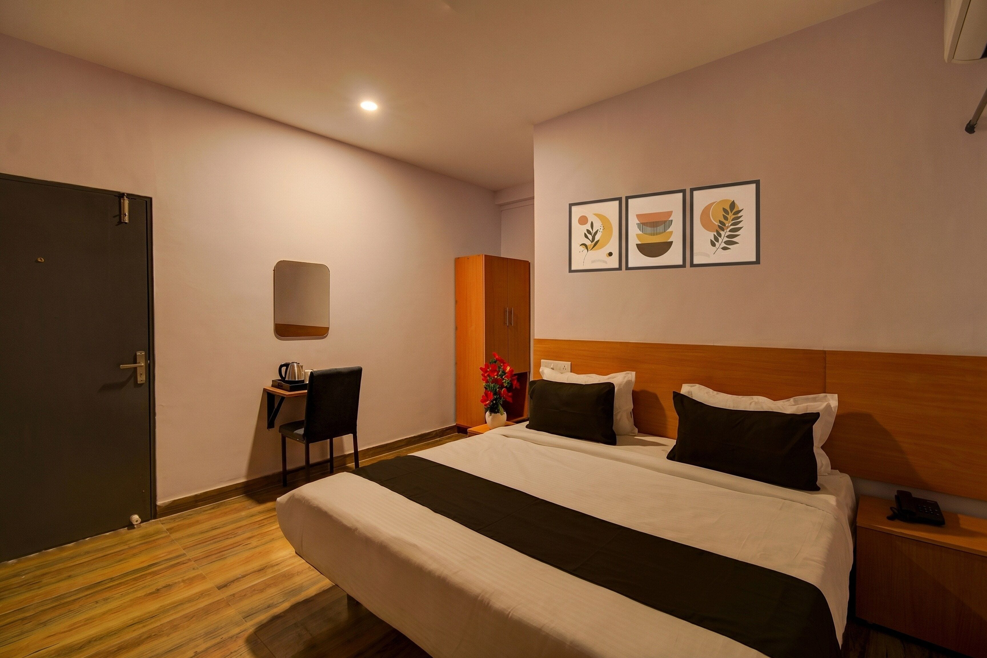 Quarto de hotel com cama, escrivaninha, cadeira, mesa de cabeceira e parede com três quadros emoldurados.