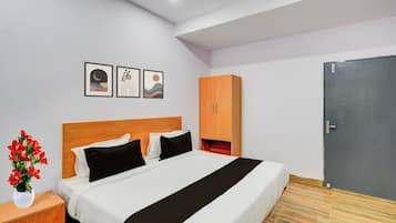 Une chambre d’hôtel avec un lit, une table de chevet, un vase de fleurs, une armoire et trois tableaux encadrés accrochés au mur.