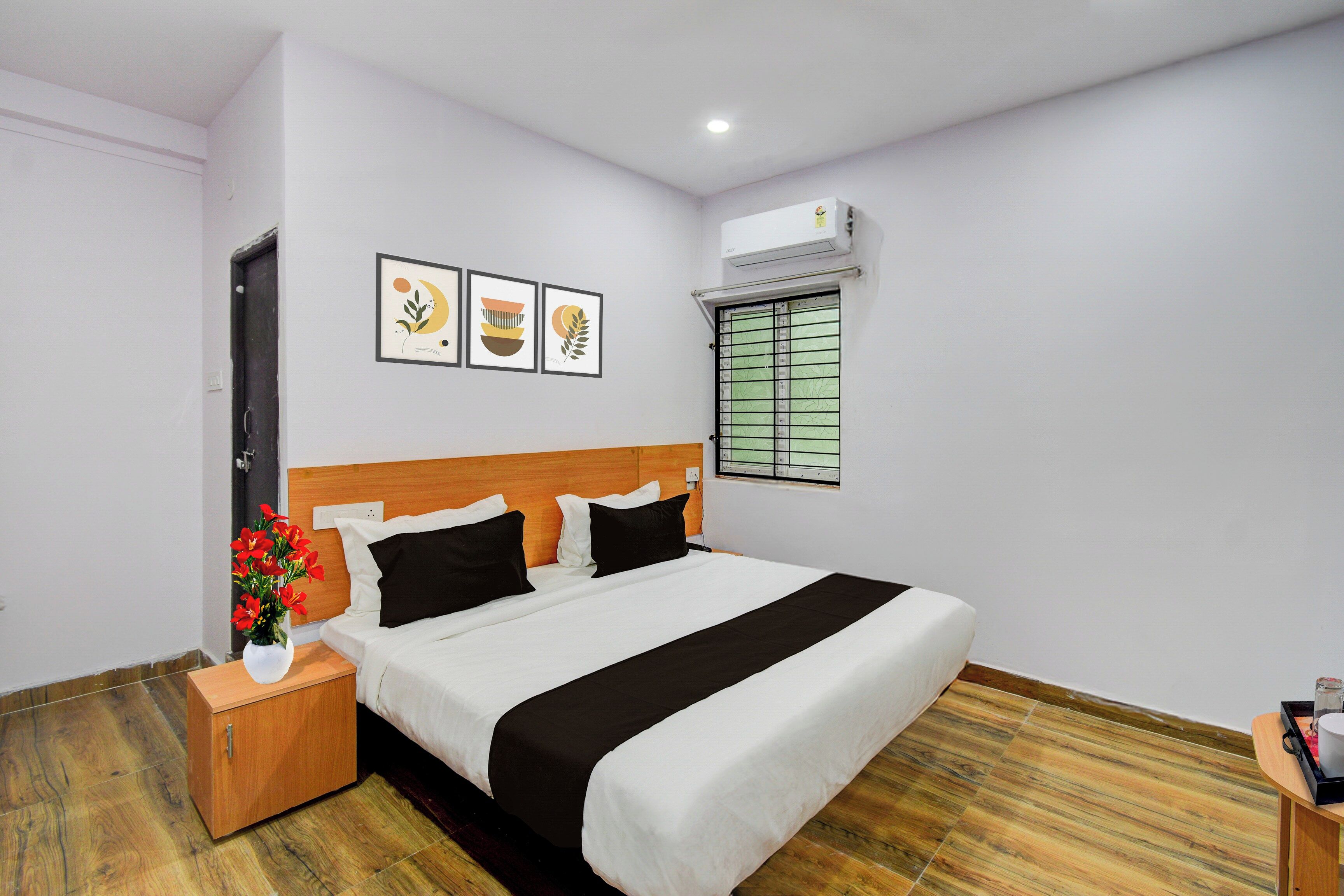 Une chambre d ’hôtel avec un lit, une table de chevet, un vase de fleurs et une fenêtre avec des stores.