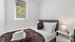 Une chambre à coucher avec un lit, une table de chevet, une lampe et une fenêtre avec des stores.