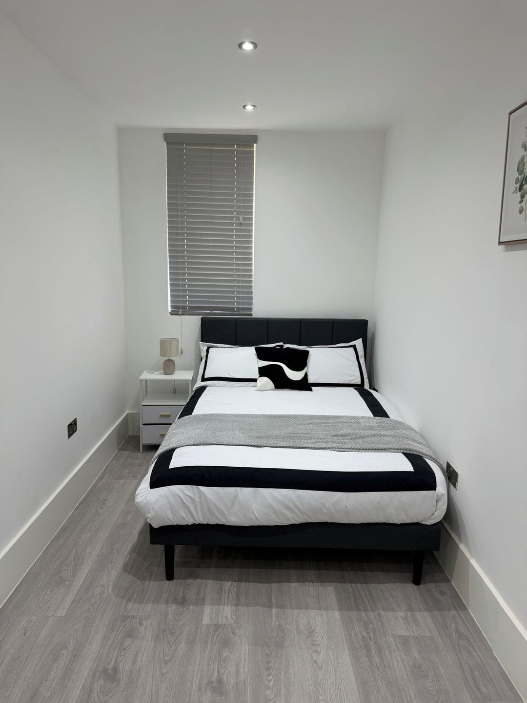 A bedroom with a bed, bedside table, lamp, and a window with blinds.