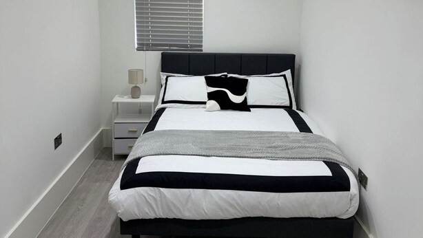 Une chambre à coucher avec un lit, une table de chevet, une lampe et une fenêtre avec des stores.