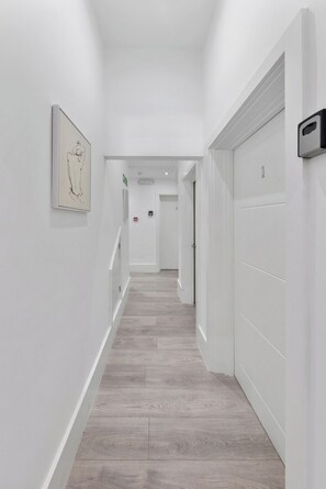 A hallway with a wooden floor, white walls, and a framed artwork on the left.