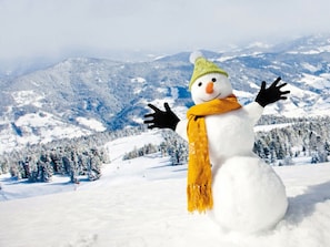 A snowman with a green hat and yellow scarf standing in a snowy landscape with mountains in the background. - One-bedroom Cabin (Sankt Georgen am Kreischberg)