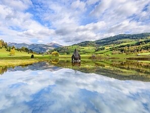 A tranquil lakeside scene with a wooden cabin, surrounded by lush greenery and distant mountains. - One-bedroom Cabin (Sankt Georgen am Kreischberg)