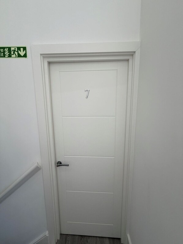 A white door with the number 7, a door handle, and a green emergency exit sign on the wall.