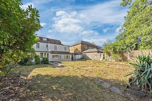 A residential property with a fenced backyard, a pathway leading to the house, and mature trees.