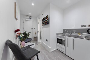 A modern kitchen with white cabinets, a microwave, and a sink. There is a vase with flowers on a table.