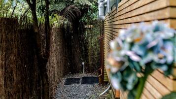 A narrow pathway leading to a wooden structure with a metal grate and a small post.