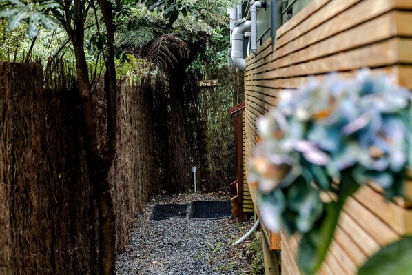 A narrow pathway leading to a wooden structure with a metal grate and a small post.