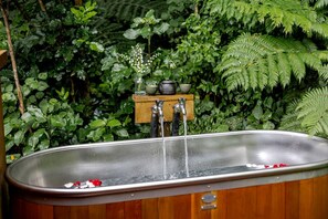 A wooden bathtub with a faucet and a wooden shelf above it.