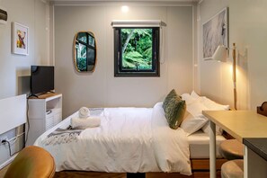 Une chambre d’hôtel équipée d’un lit, d’un bureau, d’une télévision, d’une fenêtre donnant sur un espace verdoyant et d’œuvres d’art accrochées aux murs.