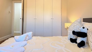 Un dormitorio con cama, armario, lámpara y un peluche de panda.