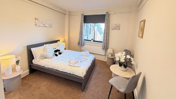 Un dormitorio con cama, mesitas de noche, una silla, una ventana con cortinas y un radiador.
