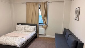 Un dormitorio con cama, sofá, ventana con cortinas y radiador.