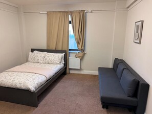 Et soveværelse med seng, sofa, et vindue med gardiner og en radiator.