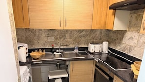 Una cocina compacta con armarios de madera, horno empotrado, lavadora y lavaplatos.