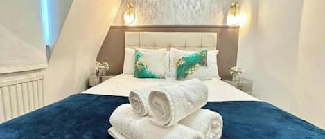 Une chambre d’hôtel avec un lit, deux tables de chevet et un luminaire fixé au mur.