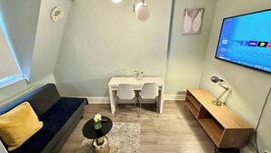 Una sala de estar moderna con un sofá, una mesa de comedor con sillas, una pequeña mesa de centro, un televisor montado en la pared y una mesita auxiliar de madera.