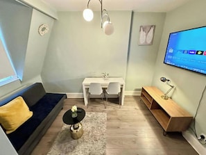 En moderne stue med sofa, spisebord med stole, lille sofabord, fjernsyn ophængt på væggen og et træ sidebord.