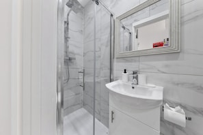 A modern bathroom with a glass-enclosed shower, a white sink, and a mirror with a framed reflection.