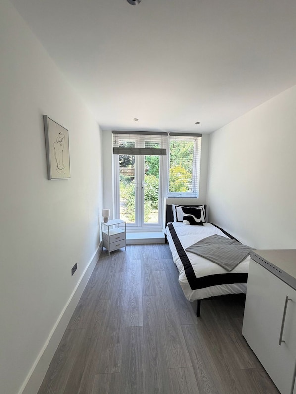 A modern bedroom with a bed, bedside table, and a window with a view of greenery.
