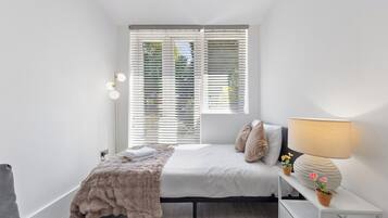 Een moderne slaapkamer met een bed, nachtkastje, lamp en uitzicht door het raam.