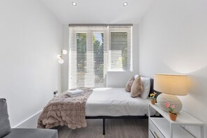 A modern bedroom with a bed, bedside table, lamp, and a view through the window.