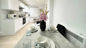 Una cocina moderna con armarios blancos, un microondas y una zona de comedor con una mesa para dos.