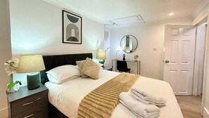 Una habitación de hotel con cama, mesitas de noche, escritorio, silla, espejo y puerta.