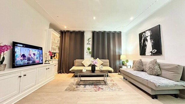 Una sala de estar moderna con un televisor de pantalla plana, un sofá, una mesa de centro y una zona de comedor con armarios.