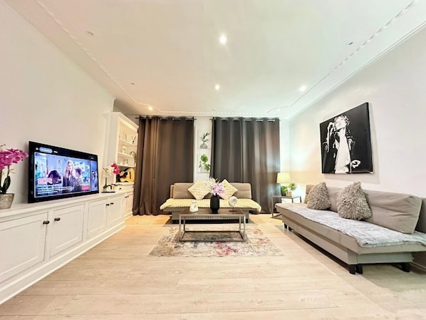 En moderne stue med fjernsyn, sofa, sofabord og et spiseområde med skabe.
