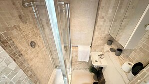 Un baño pequeño con ducha, inodoro, lavabo y un espejo.