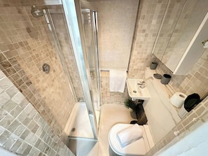 Et lille badeværelse med bruser, toilet, vask og et spejl.