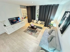 En moderne stue med et fladskærms-TV, en sofa, et sofabord og en bogreol.