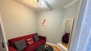 Una sala pequeña con un sofá rojo, una mesa de centro redonda y un espejo.